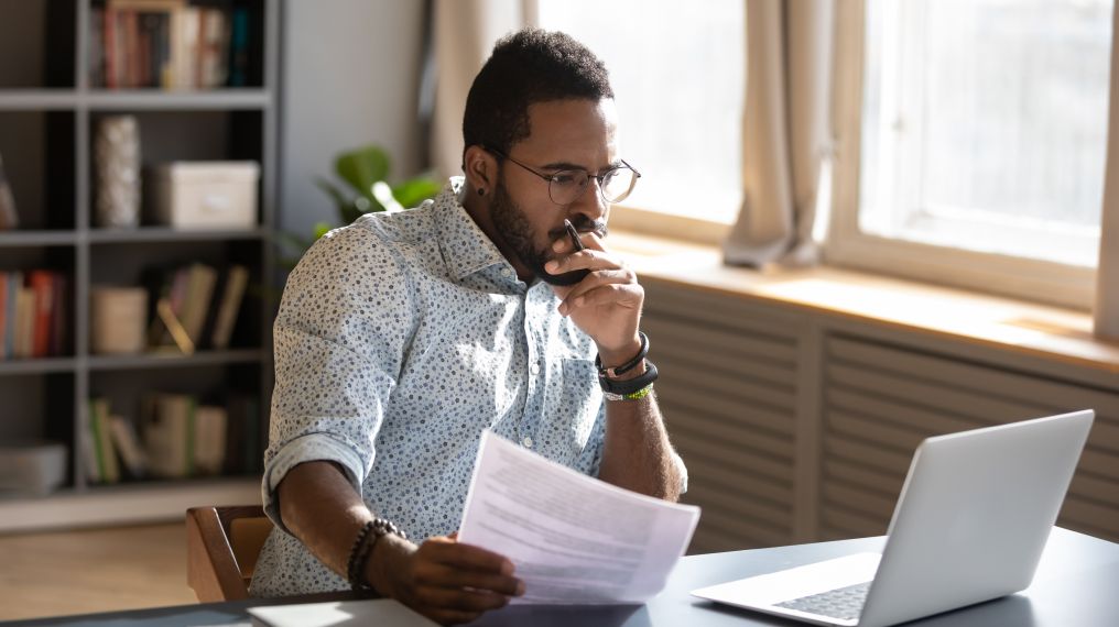 Person at home working on a laptop studying paper documents